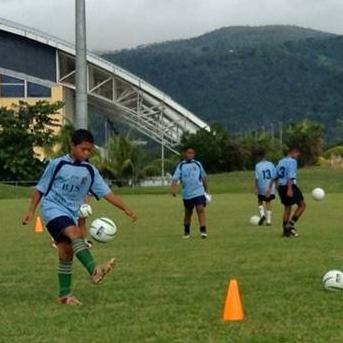 A Projects Abroad volunteer coaching sports in Samoa plays football with a group of children at a local school. Children do football drills during a training session led by a Projects Abroad volunteer sports coach in Samoa.
